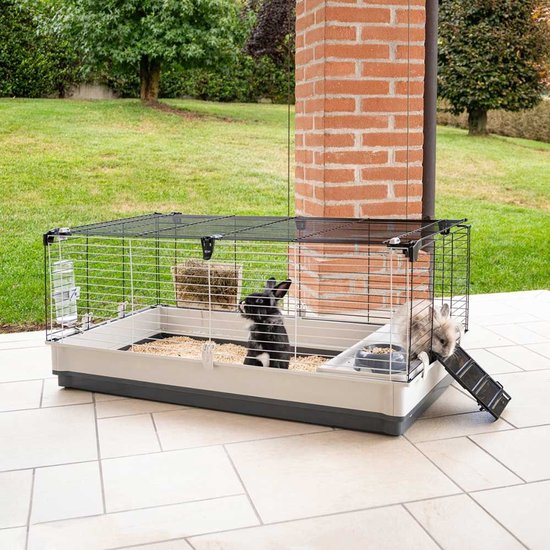 Twee konijnen in Krolik Extra Large kooi buiten op een terras, met een hellingbaan.