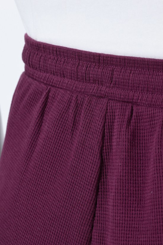 Detail van de tailleband van een donkerpaarse sweatculotte met elastiek en rimpels.