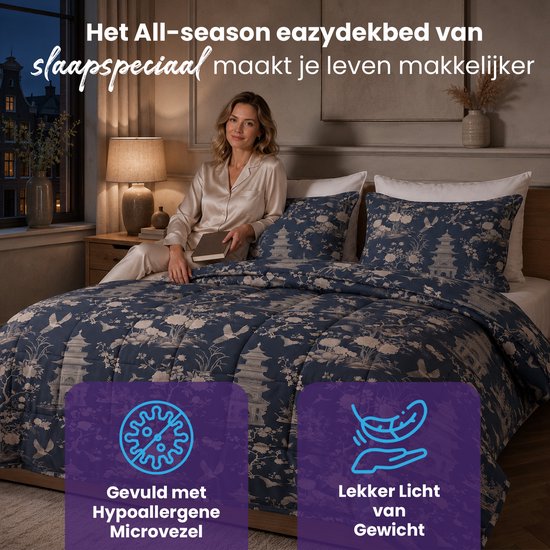Vrouw in satijnen pyjama op een bed met een blauw dekbed met pagode- en bloemenprint.