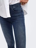 Close-up van de zak en slijtplekken op de blauwe skinny jeans, gedragen met wit overhemd.