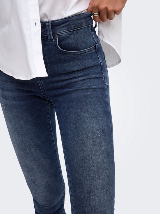 Close-up van de zak en slijtplekken op de blauwe skinny jeans, gedragen met wit overhemd.