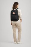 Vrouw draagt een zwarte Fjällräven Kånken laptoprugzak met een rond rood Fjällräven logo op de voorkant.
