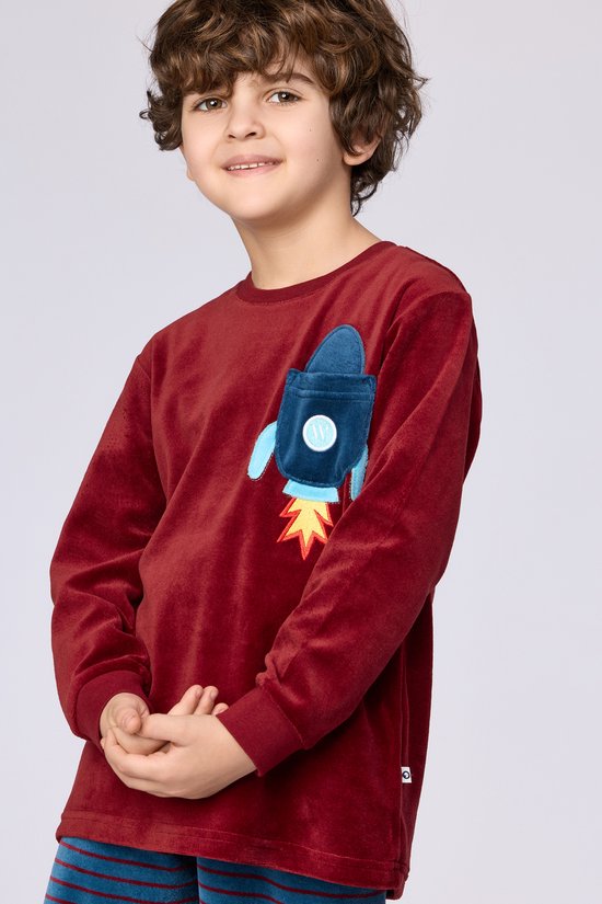Garçon portant un haut de pyjama en velours bordeaux avec une application de fusée bleue sur la poitrine.