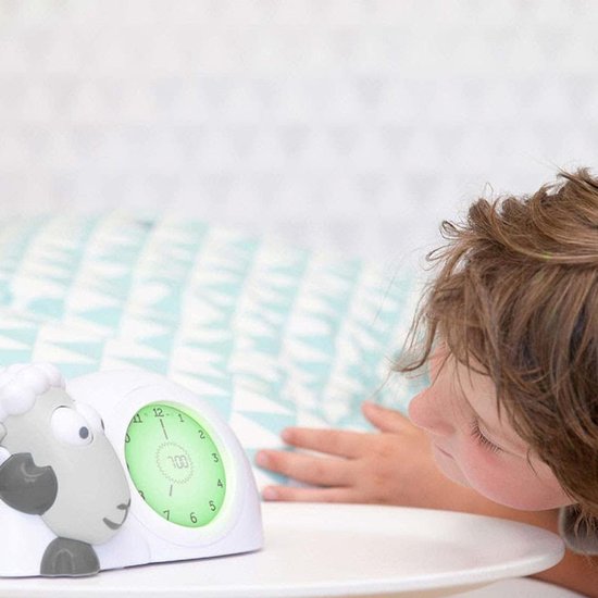 Kind kijkt naar grijze schaap wekker met groene verlichting.