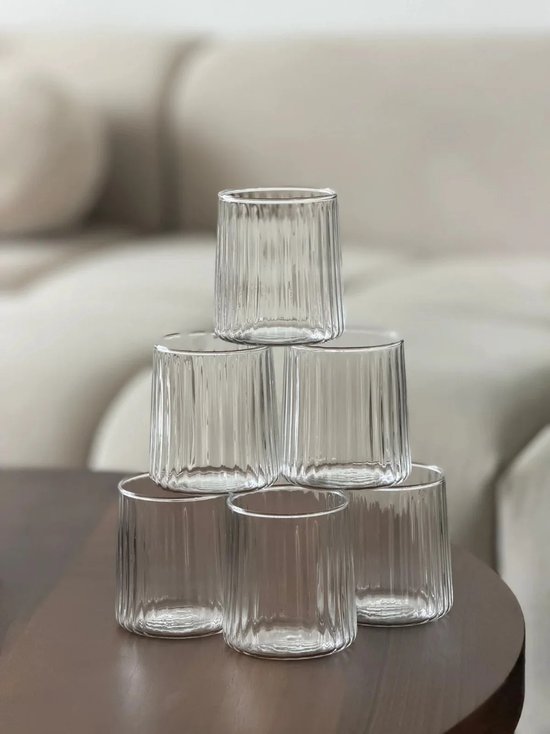 Pile de six verres transparents côtelés, sur une table brun foncé.