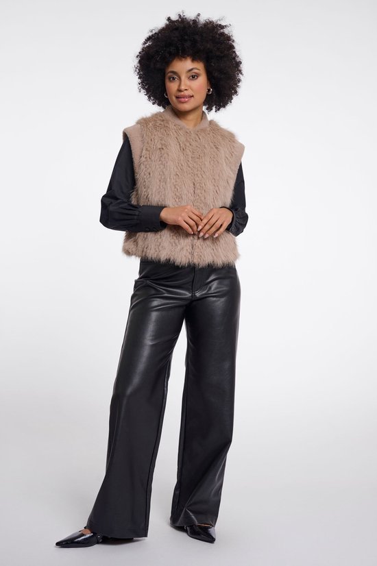 Model met bruin pluizig vest, zwart overhemd en zwarte leren broek.