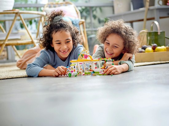 Twee lachende kinderen liggen op de grond en spelen met een LEGO Friends café set.