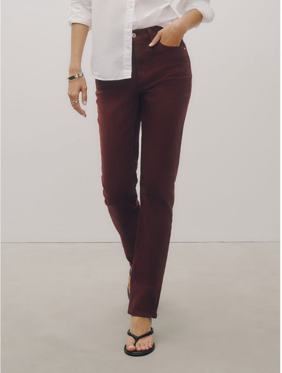 Model in een donkerrode slim-fit stretchjeans en wit overhemd, gecombineerd met zwarte sandalen.