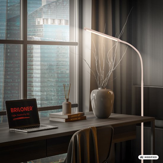 Een beige vloerlamp met gebogen arm, die een bureau met een laptop, boeken en decoratie verlicht bij een raam met uitzicht op de stad.