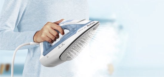Wit en blauw Tefal Virtuo 30 stoomstrijkijzer met stoom uit de zoolplaat, in handen van een persoon met een lichtblauwe trui.