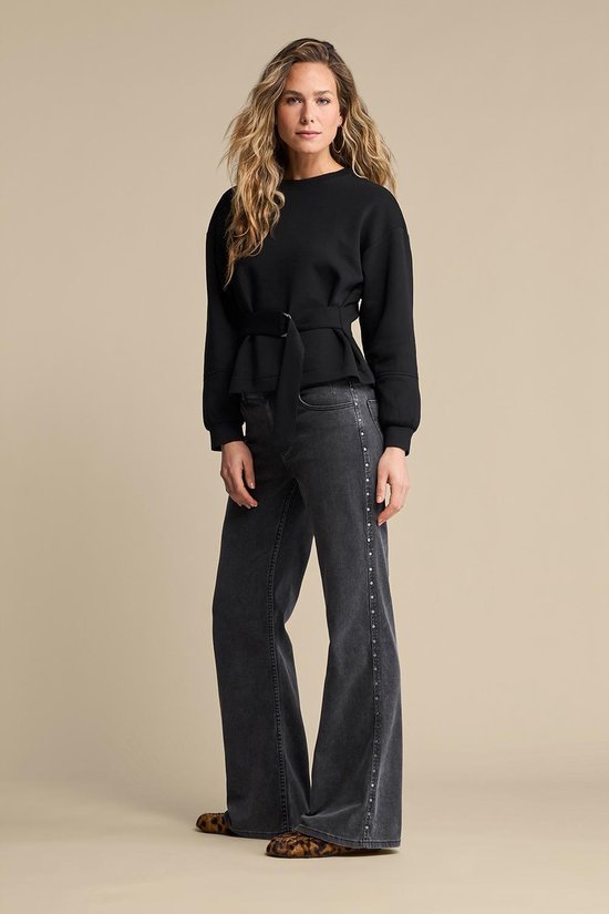 Model draagt zwarte sweater met ceintuur en jeans.