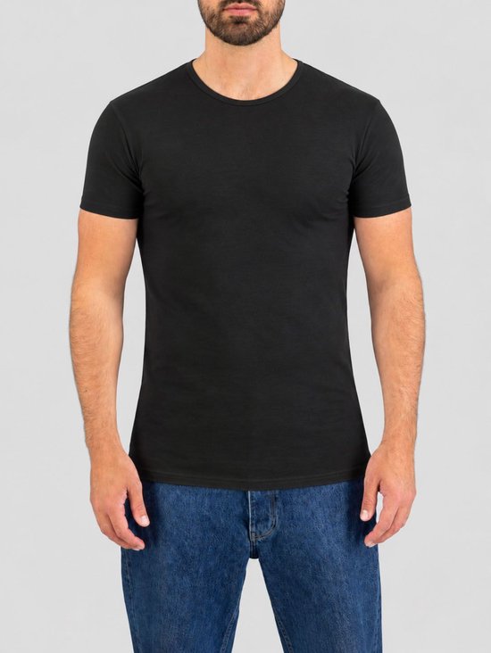 Model draagt een nauwsluitend zwart T-shirt met ronde hals en korte mouwen, gecombineerd met een blauwe spijkerbroek.