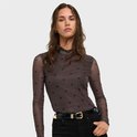 Model draagt een bruine mesh top met hartjesprint, hoge hals, en zwarte broek met riem.