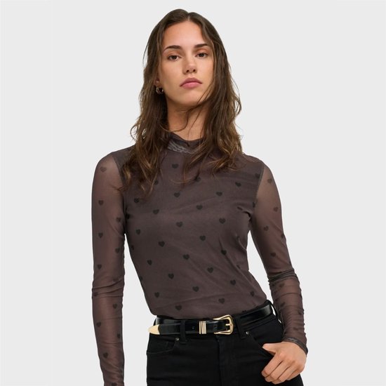 Model draagt een bruine mesh top met hartjesprint, hoge hals, en zwarte broek met riem.