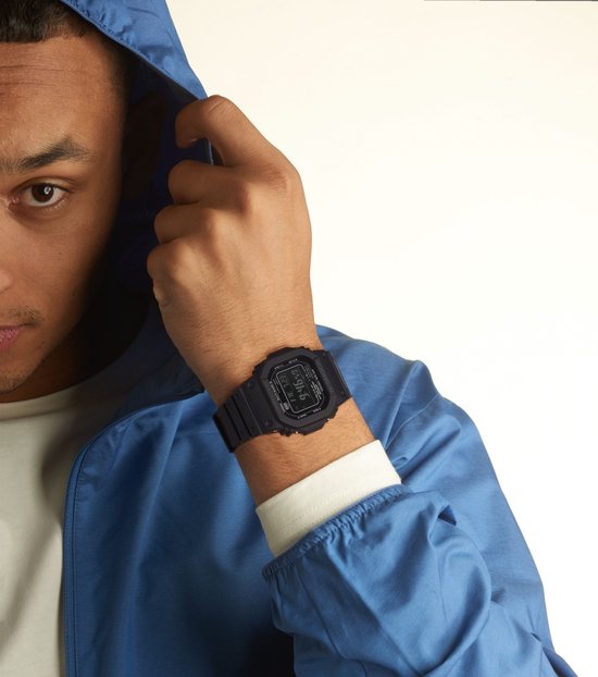 Model draagt een zwart G-Shock horloge met digitale wijzerplaat om de pols. Blauwe hoodie met capuchon.