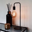 Zwarte minimalistische tafellamp met een zichtbare warme LED-gloeidraad, naast een zwarte geurstokjeshouder.
