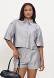 Model in zilverkleurige, glanzende cropped blouse met korte mouwen, bijpassende shorts en zwarte laarzen.
