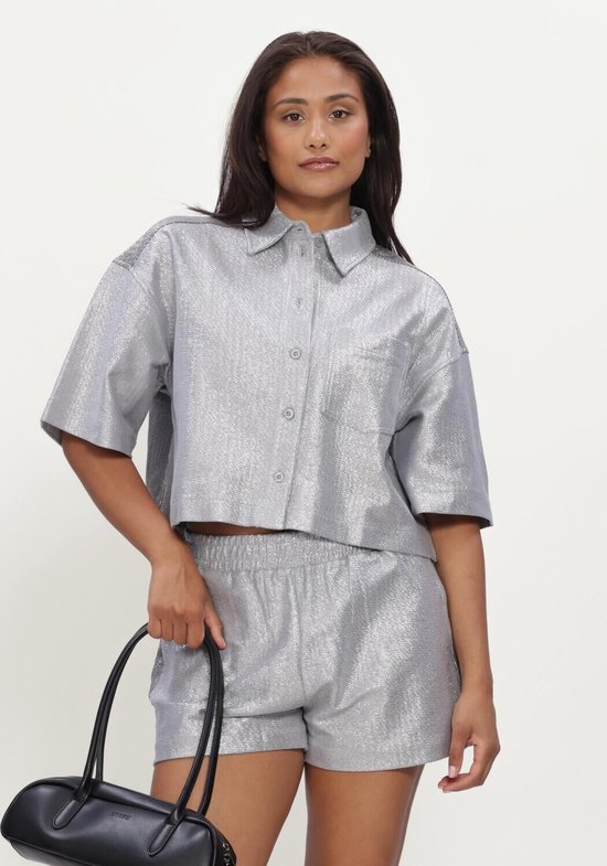 Model in zilverkleurige, glanzende cropped blouse met korte mouwen, bijpassende shorts en zwarte laarzen.
