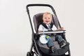 Een vrolijke baby zit in een grijze kinderwagen met een blauwe muziekmobiel eraan.