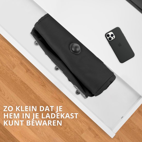 Opvouwbare zwarte reistas, klein genoeg voor in een lade, naast een telefoon.