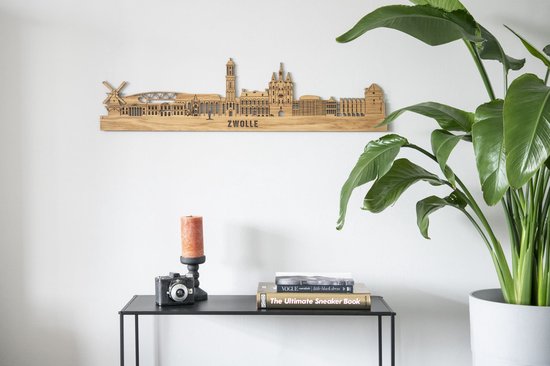 Houten skyline van Zwolle, opgehangen aan een witte muur boven een boekenplank.