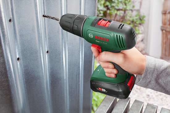 Hand met Bosch boormachine boort in een metalen plaat. Boormachine is groen en zwart met rode details.