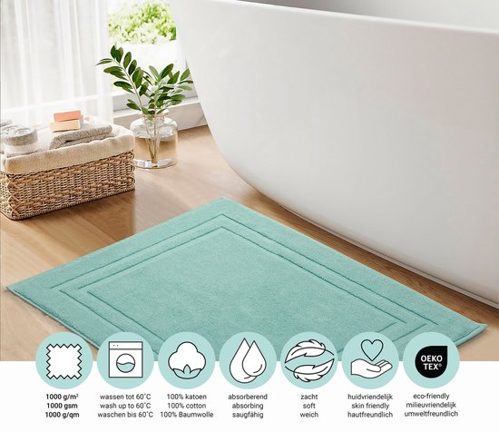 Tapis de bain turquoise avec double bord festonné, à côté d'une baignoire. Les icônes indiquent 1000 g/m², lavable à 60°C, 100% coton, absorbant, doux, hypoallergénique et Oeko-Tex.