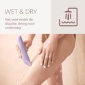 Vrouw gebruikt paarse lady shaver onder de douche.