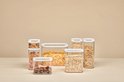 Différentes tailles de boîtes de conservation transparentes remplies de céréales et de fruits secs.