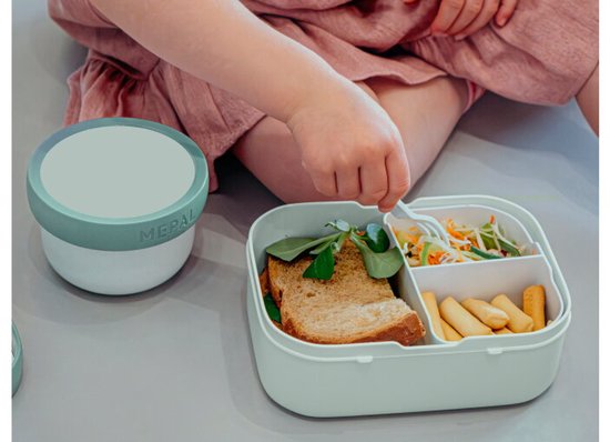 Un enfant portant une robe prend une salade dans une boîte à lunch vert d'eau avec compartiment bento.