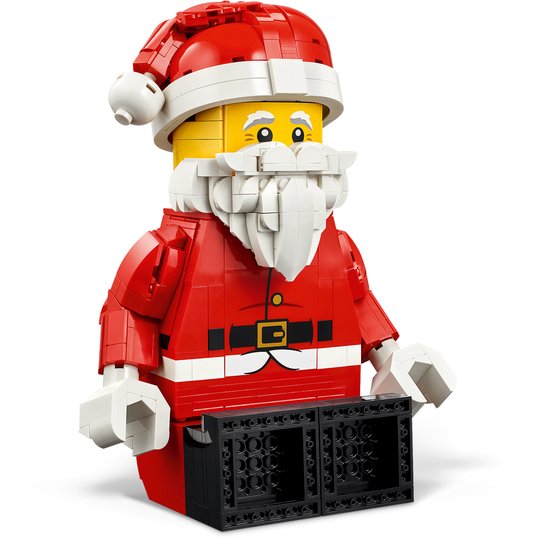 LEGO opgeschaalde Kerstman minifiguur in rood pak, staand op een tafel onder een kerstboom.
