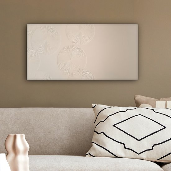 Beige canvas met cirkelvormige patronen, hangend boven een bank met een vaas op de achtergrond.