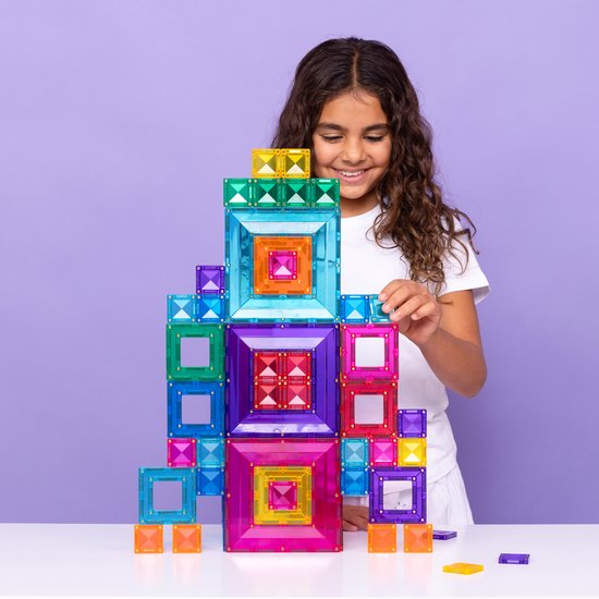 Meisje met krullend haar dat een hoge, gekleurde, magnetische Connetix toren bouwt.