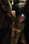 Jongen met een groene hoofdlamp die zich een weg baant tussen rotsen.
