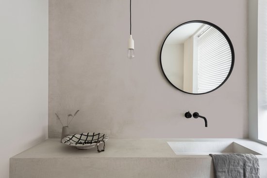 Een aanrecht in een badkamer met een betonnen wastafel, een zwarte kraan en een ronde spiegel aan de muur.