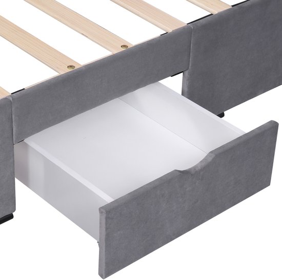 Detail van een open opberglade van een grijs gestoffeerd bedframe, met houten lattenbodem.
