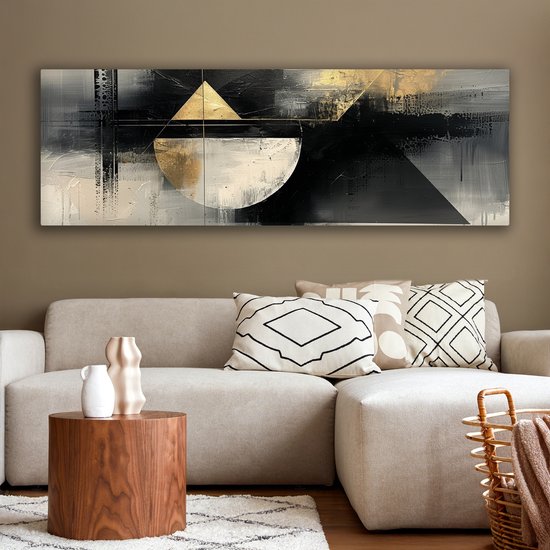 Abstract schilderij met geometrische vormen in zwart, wit en goud, hangend boven een lichte bank.