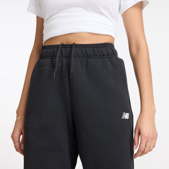 Detailopname van de tailleband van een donkere joggingbroek met trekkoord en het witte New Balance logo op de linkerheup.