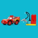 Rode LEGO Duplo Lightning McQueen auto naast een rode, blauwe en gele brandstofpomp met zwarte slang.