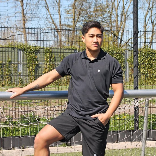 Man in zwart Donnay poloshirt en zwarte short, leunend op een hek.