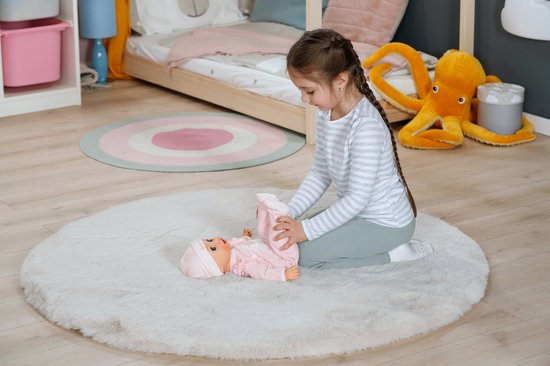 Meisje op een rond kleed kleedt een baby pop aan. Baby Annabell.