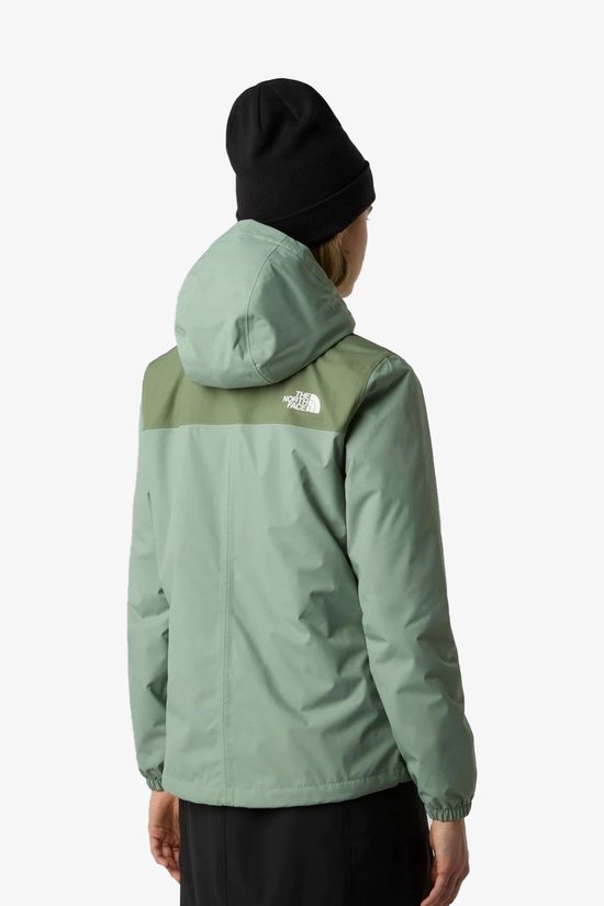 Vrouw met zwarte muts draagt een lichtgroene jas met donkergroene schouderaccenten. The North Face logo op de rug.