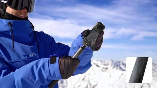 Man in blauwe ski-jas met skibril, houdt een zwarte Insta360 actioncam vast op een verlengstuk. Berglandschap met sneeuw.