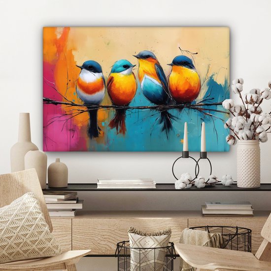 Vier kleurrijke vogels op een tak, hangend aan een muur boven een dressoir. De achtergrond is een abstracte mix van oranje, roze, blauw en geel. Naast de kast staan decoraties.