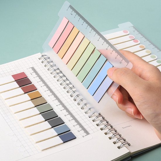 Hand houdt transparante sticky notes met liniaal vast, in pastelkleuren, boven een notitieboek.