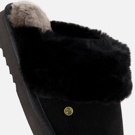 Zwarte suède pantoffel met dikke zwarte en grijze schapenvachtvoering en een goudkleurig logo.