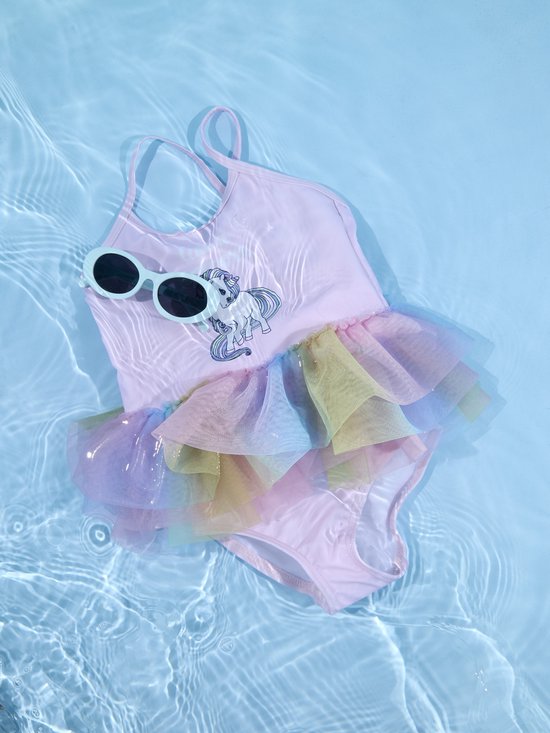 Roze badpak met 'like a unicorn' print en regenboog tule rokje, met zonnebril, in water.