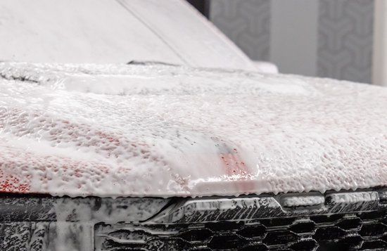 Een rode auto bedekt met witte autoshampoo schuim, met een grille zichtbaar.