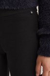 Detail van een zwarte legging met een klein wit sterretje op een zwart label bij de tailleband, naast een donkerblauwe pluizige trui.