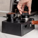 Hand draait aan houten tamper bovenop zwarte barista tamper station.
